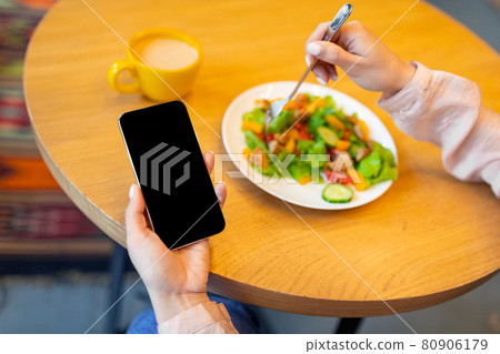 Healthy food and diet planning concept. Woman using smartphone with black screen and eating fresh salad in cafe 80906179