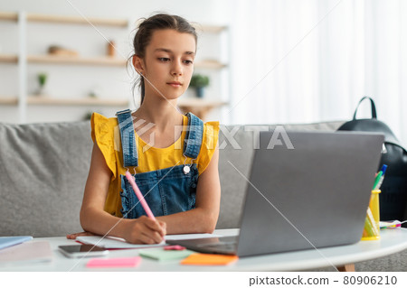Girl sitting at table, using laptop, writing in notebook Girl sitting at table, using laptop, writing in notebook 80906210