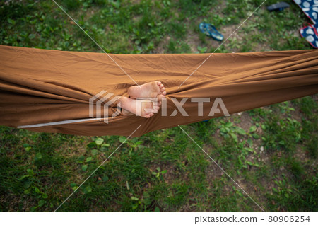 Two child feet looking out a brown hammock 80906254