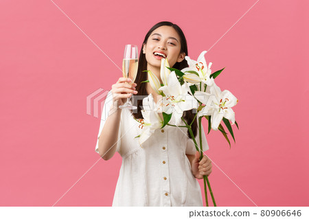 Celebration, party holidays and fun concept. Smiling pretty glamour asian woman in dress with white lilies bouquet, raising glass of champagne to make toast, drink for birthday girl Celebration, party holidays and fun concept. Smiling pretty glamour asian woman in dress with white lilies bouquet, raising glass of champagne to make toast, drink for birthday girl 80906646