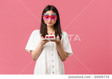 Celebration, party holidays and fun concept. Dreamy cute birthday girl in funny sunglasses holding b-day cake and gazing at candle thoughtful, making wish, standing pink background 80906739