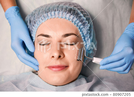 Beautician massaging woman forehead with facial massager. Beautician massaging woman forehead with facial massager. 80907205