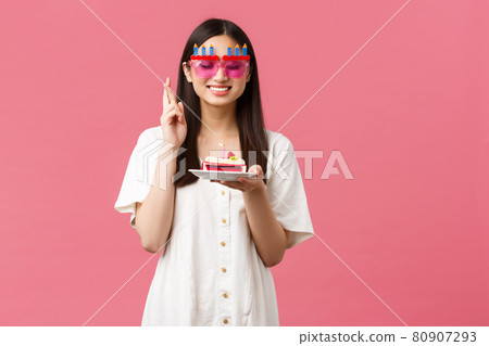 Celebration, party holidays and fun concept. Smiling happy birthday girl making wish on b-day cake, close eyes and cross fingers good luck, want dream come true, pink background Celebration, party holidays and fun concept. Smiling happy birthday girl making wish on b-day cake, close eyes and cross fingers good luck, want dream come true, pink background 80907293