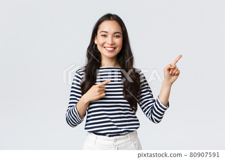 Lifestyle, beauty and fashion, people emotions concept. Good-looking young female in striped shirt pointing fingers right, inviting customers, advertise special discount, smiling at camera happy Lifestyle, beauty and fashion, people emotions concept. Good-looking young female in striped shirt pointing fingers right, inviting customers, advertise special discount, smiling at camera happy 80907591
