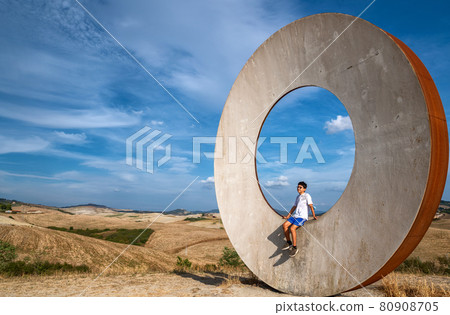 Volterra, Tuscany, Italy. August 2020. In the countryside of the city, a modern art installation draws attention to the Tuscan landscape. A young tourist interacts with the installation. Volterra, Tuscany, Italy. August 2020. In the countryside of the city, a modern art installation draws attention to the Tuscan landscape. A young tourist interacts with the installation. 80908705