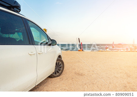 Side view of big family white suv van car with big rooftop cargo rack box at scenic sand seaside campsite camp coast of sea or ocean sky on background. Accessory rental travel trip vacation concept Side view of big family white suv van car with big rooftop cargo rack box at scenic sand seaside campsite camp coast of sea or ocean sky on background. Accessory rental travel trip vacation concept 80909051