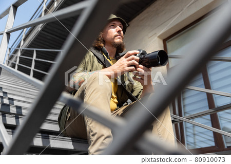 Portrait of young man, photographer, cameraman with professional camera, equipment during working summer day outdoors. Concept of occupation, job, education Portrait of young man, photographer, cameraman with professional camera, equipment during working summer day outdoors. Concept of occupation, job, education 80910073