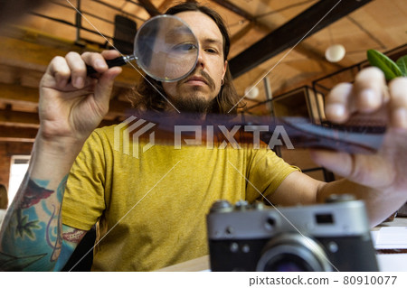 One young Caucasian man, photographer, cameraman with professional camera, equipment during working at office, indoors. Concept of occupation, job, education One young Caucasian man, photographer, cameraman with professional camera, equipment during working at office, indoors. Concept of occupation, job, education 80910077