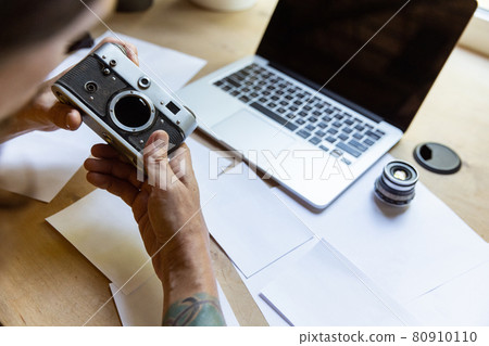 One young Caucasian man, photographer, cameraman with professional camera, equipment during working at office, indoors. Concept of occupation, job, education 80910110