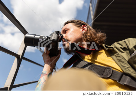 Portrait of young man, photographer, cameraman with professional camera, equipment during working summer day outdoors. Concept of occupation, job, education Portrait of young man, photographer, cameraman with professional camera, equipment during working summer day outdoors. Concept of occupation, job, education 80910125