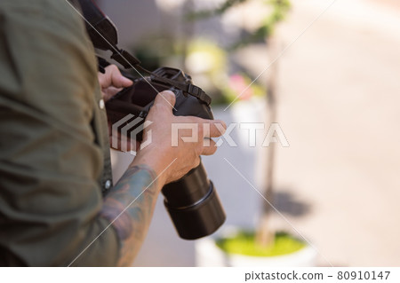 Close-up of young man, photographer, cameraman with professional camera, equipment during working summer day outdoors. Concept of occupation, job, education Close-up of young man, photographer, cameraman with professional camera, equipment during working summer day outdoors. Concept of occupation, job, education 80910147