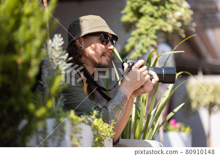 Portrait of young man, photographer, cameraman with professional camera, equipment during working summer day outdoors. Concept of occupation, job, education Portrait of young man, photographer, cameraman with professional camera, equipment during working summer day outdoors. Concept of occupation, job, education 80910148