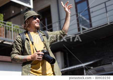 Portrait of young man, photographer, cameraman with professional camera, equipment during working summer day outdoors. Concept of occupation, job, education Portrait of young man, photographer, cameraman with professional camera, equipment during working summer day outdoors. Concept of occupation, job, education 80910150