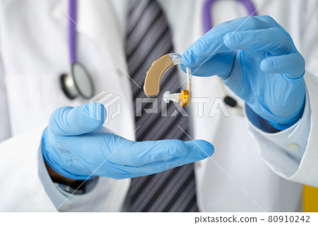 Otorhinolaryngologist holding hearing aid with rubber gloves closeup 80910242
