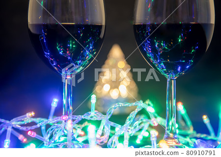 two glasses on the background of a shining Christmas tree and a multi-colored garland on a dark night background. New Year celebration. 80910791