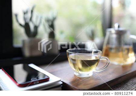 Tea in clear glass cup and teapot on wooden board with phone and notebook Tea in clear glass cup and teapot on wooden board with phone and notebook 80911274