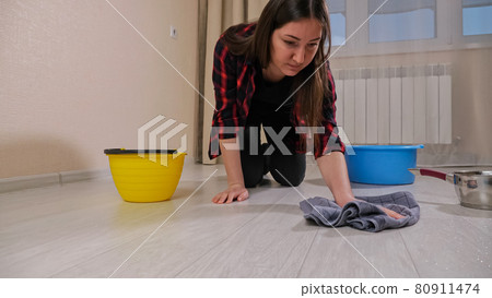 Disappointed lady wipes water with rug from floor in room 80911474
