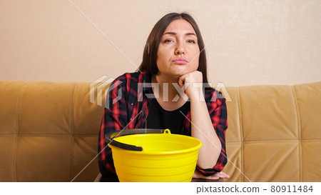 Emotional woman collects water into bucket sitting on sofa Emotional woman collects water into bucket sitting on sofa 80911484