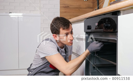 Skilled employee twists screw on broken oven repairing Skilled employee twists screw on broken oven repairing 80911538