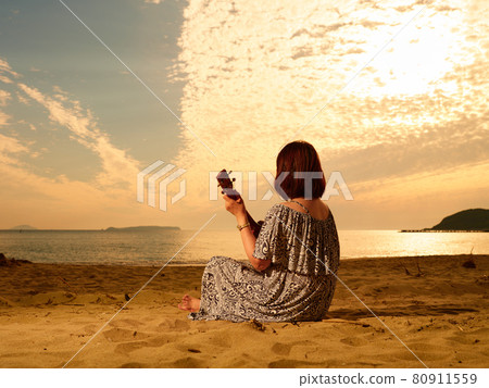 Back view of a woman playing the ukulele on a sandy beach Back view of a woman playing the ukulele on a sandy beach 80911559