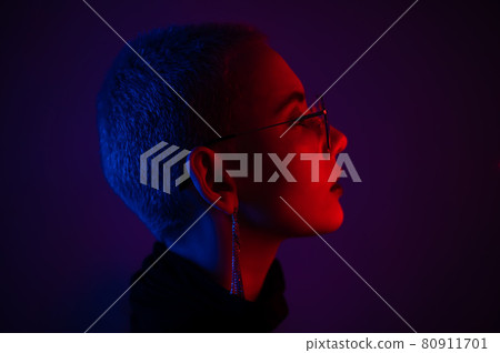 Portrait of beautiful young woman with short hair wearing glasses in neon light 80911701