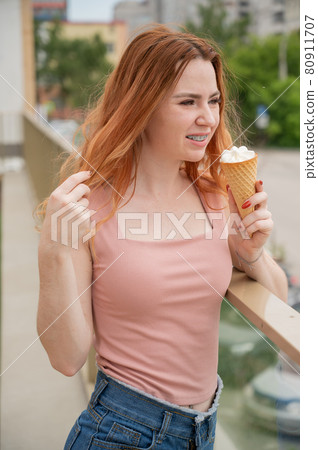 Portrait of young beautiful red-haired woman smiling with braces and going to eat ice cream cone outdoors in summer 80911707