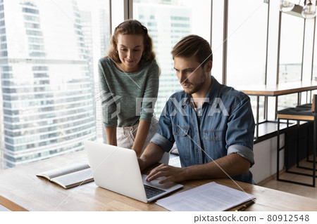 Friendly business mentor training intern, looking at laptop screen 80912548