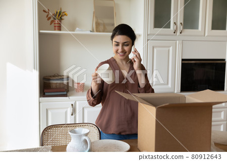 Smiling ethnic female renter unpack parcel with kitchenware Smiling ethnic female renter unpack parcel with kitchenware 80912643