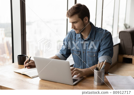 Serious businessman, employee, entrepreneur working at laptop and writing Serious businessman, employee, entrepreneur working at laptop and writing 80912717
