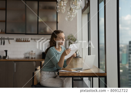 Happy young woman reading paper letter at home workplace Happy young woman reading paper letter at home workplace 80912722
