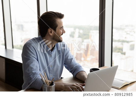 Happy confident thoughtful businessman using laptop, looking out office window 80912985