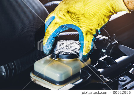 The mechanic hand is open or close the cap of the power steering fluid to check the hydraulic fluid level 80912996