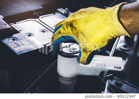 The mechanic hand is open or close the cap of windshield washer fluid reservoir tank to check the fluid level 80912997