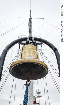 Golden ship's bell with blue rope against the mast and gray sky, Golden ship's bell with blue rope against the mast and gray sky, 80913260