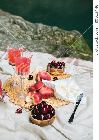 Cozy summer picnic near the lake with wine, cherry, peaches, brie cheese, camamber. Romantic picnic for Valentine's Day on February 14. 80913446