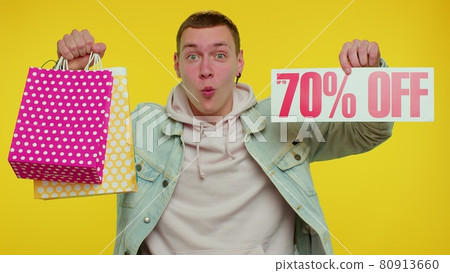 Cheerful teen man showing shopping bags and Up To 70 Percent Off inscriptions banner, Black Friday 80913660