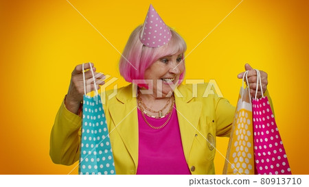 Elderly granny woman showing shopping bags, advertising discounts, looking amazed with low prices Elderly granny woman showing shopping bags, advertising discounts, looking amazed with low prices 80913710