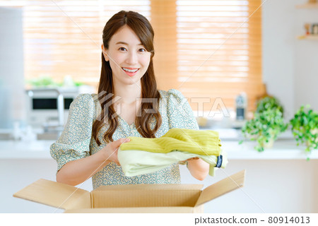Young housewife packing clothes in cardboard in the living room 80914013