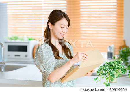 Young housewife opening mail luggage in the kitchen Young housewife opening mail luggage in the kitchen 80914034