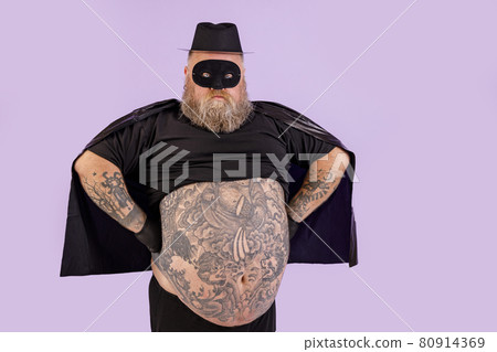 Confident man with overweight in Zorro suit holds hands on waist on purple background 80914369