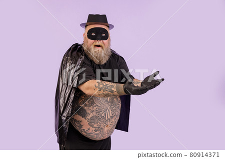 Emotional plus size man in black hero suit shows on something on purple background Emotional plus size man in black hero suit shows on something on purple background 80914371
