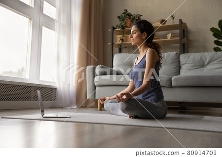 Mindful woman meditating, practicing yoga online at home, using laptop 80914701
