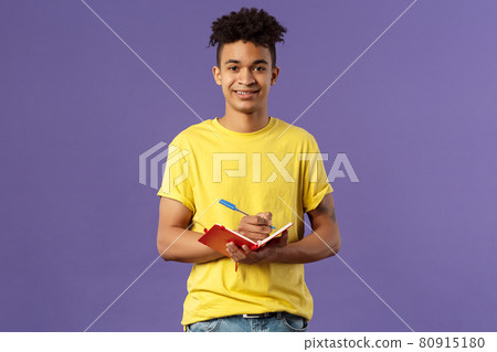 Portrait of young hispanic male student studying online courses, writing down lecture, making personal schedule or taking notes in planner, look camera enthusiastic and interested, purple background. 80915180