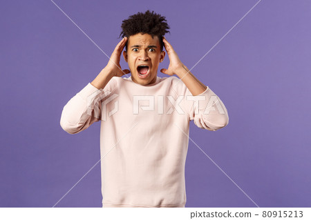 Portrait of scared and anxious young hispanic handsome man in panic, shaking hands nead head, screaming and gasping afraid, being in trouble, standing alarmed over purple background Portrait of scared and anxious young hispanic handsome man in panic, shaking hands nead head, screaming and gasping afraid, being in trouble, standing alarmed over purple background 80915213