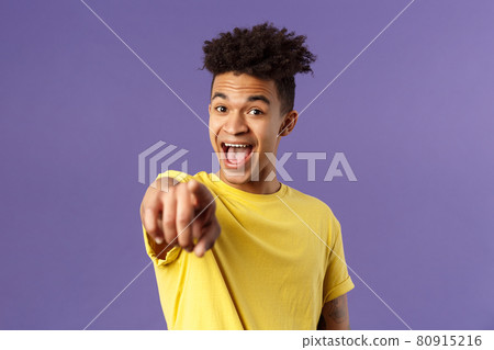Close-up portrait of upbeat, amazed hispanic man with dreads, young student pointing finger at camera and laughing, recognize someone familiar, standing purple background Close-up portrait of upbeat, amazed hispanic man with dreads, young student pointing finger at camera and laughing, recognize someone familiar, standing purple background 80915216