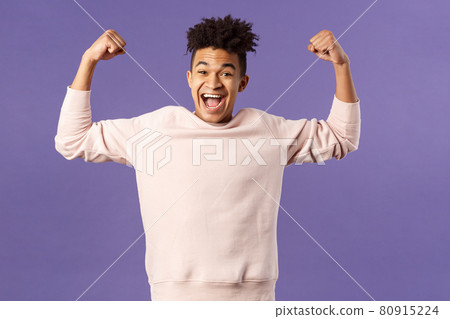 Portrait of young happy man got scholarship, applied to cool university, raise hands up flex biceps like champion, triumphing from great news, achieve goal and rejoicing, purple background 80915224