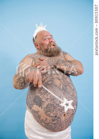 Plus size man with toy crown and magic stick poses on light blue background 80915307