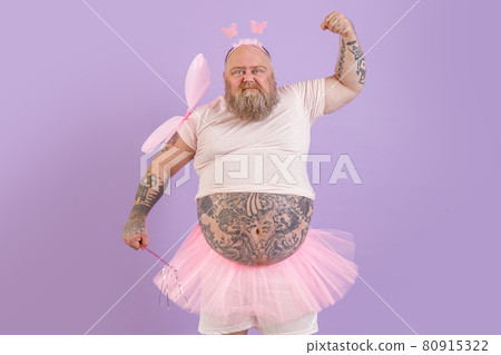Brutal obese man with tattoos in fairy costume shows muscles on purple background 80915322