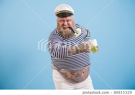 Happy plus size man in sailor suit holds delicious beer on light blue background 80915329