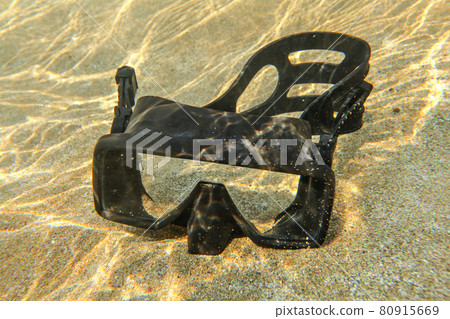 Underwater photo - light from sun refractions at black diving mask sitting in shallow water on clear sand 80915669